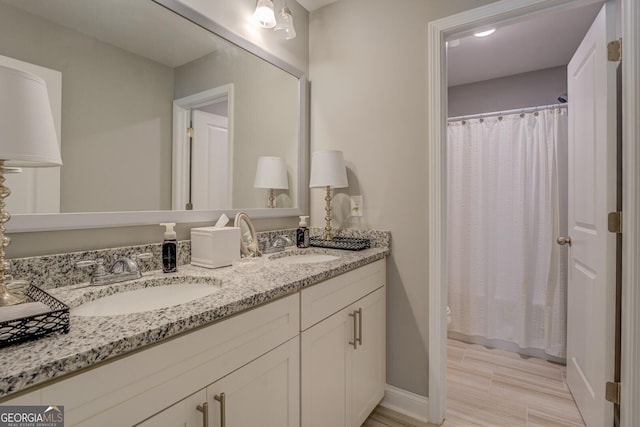 full bath featuring curtained shower, a sink, baseboards, and double vanity