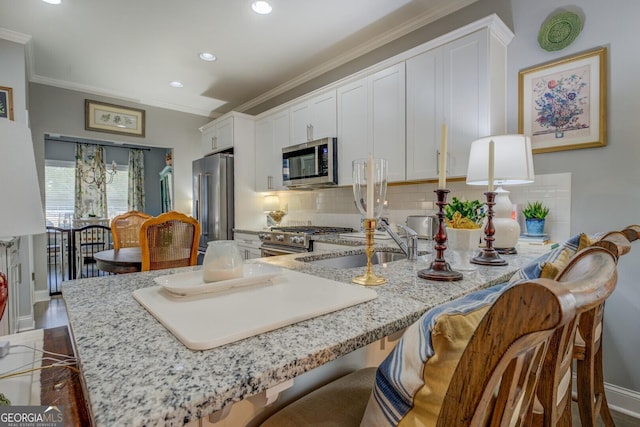 kitchen with backsplash, appliances with stainless steel finishes, ornamental molding, white cabinetry, and a sink