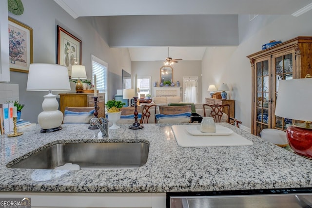 kitchen with light stone counters, open floor plan, vaulted ceiling, a sink, and dishwasher