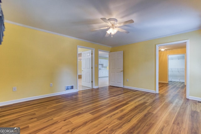 unfurnished bedroom featuring crown molding, hardwood / wood-style flooring, ceiling fan, a spacious closet, and a closet