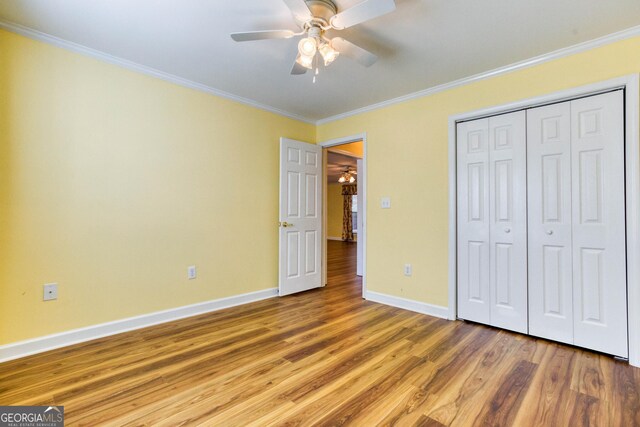 unfurnished bedroom with ceiling fan, wood-type flooring, ornamental molding, and a closet