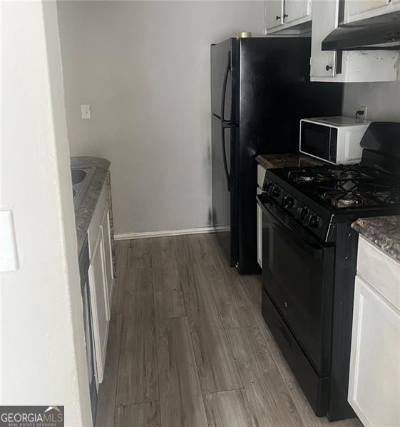 kitchen with hardwood / wood-style flooring, dark stone countertops, black gas range, and white cabinets