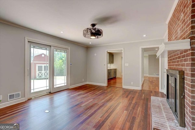 unfurnished living room featuring wood-type flooring, a brick fireplace, ceiling fan, and ornamental molding