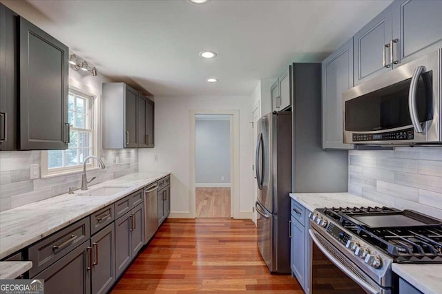 kitchen with decorative backsplash, light stone counters, stainless steel appliances, sink, and light hardwood / wood-style floors