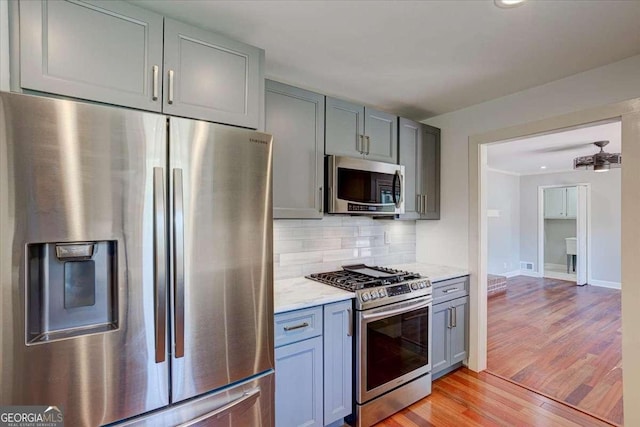 kitchen featuring gray cabinetry, backsplash, light wood-type flooring, light stone countertops, and appliances with stainless steel finishes