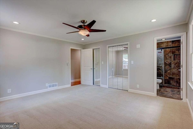 unfurnished bedroom with ensuite bath, ceiling fan, crown molding, light carpet, and two closets