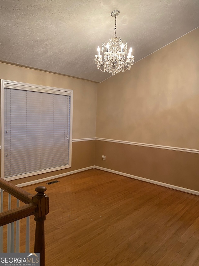 spare room with wood-type flooring, a chandelier, and a textured ceiling