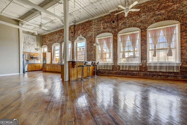 interior space featuring brick wall, ceiling fan, beam ceiling, hardwood / wood-style flooring, and a high ceiling