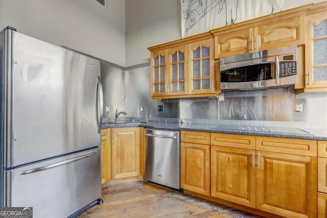 kitchen with sink, tasteful backsplash, dark stone counters, appliances with stainless steel finishes, and light wood-type flooring