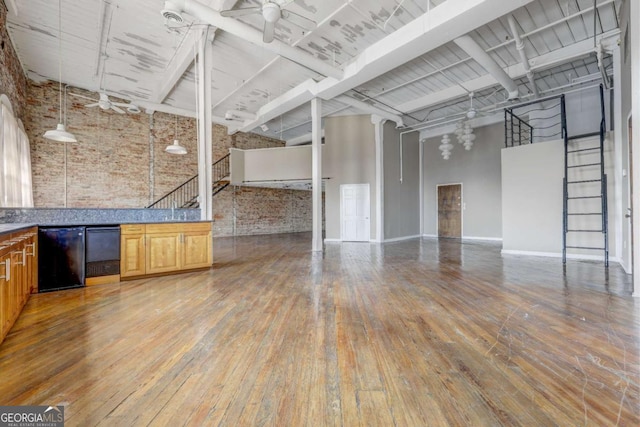 interior space with a towering ceiling, hardwood / wood-style flooring, ceiling fan, and brick wall