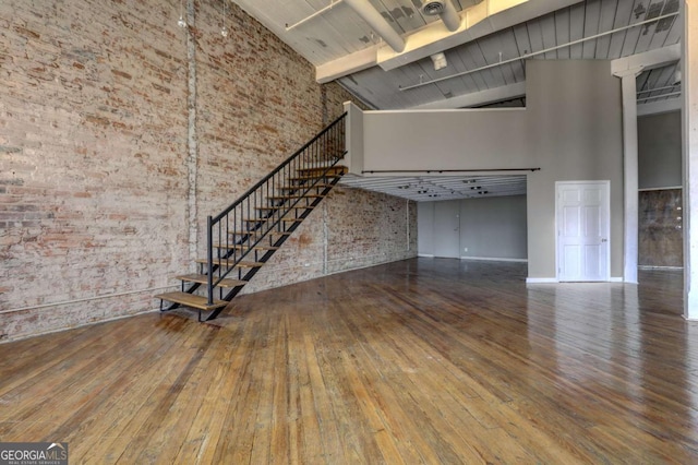 unfurnished living room with hardwood / wood-style floors, a towering ceiling, and brick wall