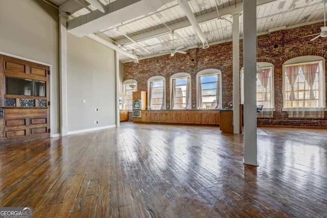 unfurnished living room featuring a towering ceiling, hardwood / wood-style flooring, ceiling fan, and brick wall