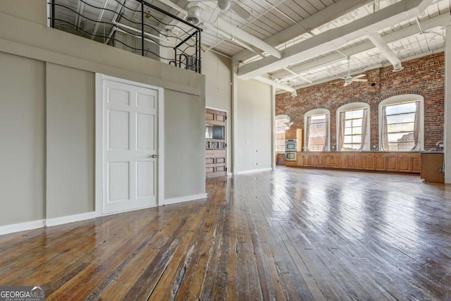 unfurnished living room with ceiling fan, a towering ceiling, brick wall, and hardwood / wood-style flooring