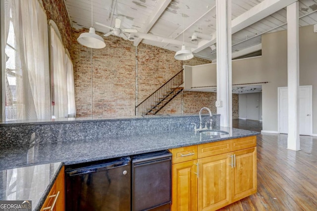 kitchen featuring dishwasher, dark stone counters, sink, a towering ceiling, and brick wall