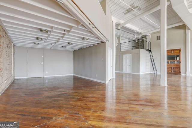 empty room featuring brick wall, a high ceiling, and wood-type flooring