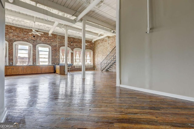 interior space featuring a high ceiling, ceiling fan, dark hardwood / wood-style floors, beamed ceiling, and brick wall