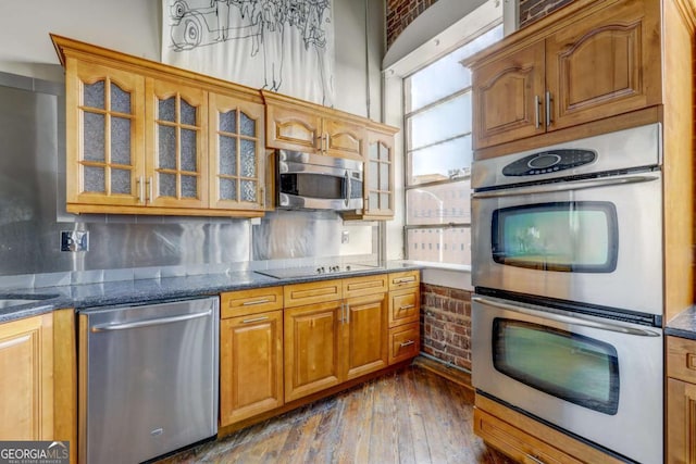 kitchen with appliances with stainless steel finishes, backsplash, dark wood-type flooring, and dark stone countertops