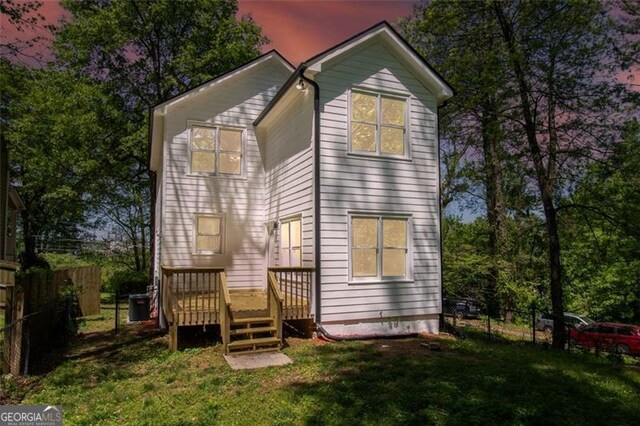 back house at dusk with a lawn, central AC unit, and a deck