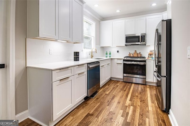 kitchen with white cabinetry, sink, light hardwood / wood-style flooring, decorative backsplash, and appliances with stainless steel finishes