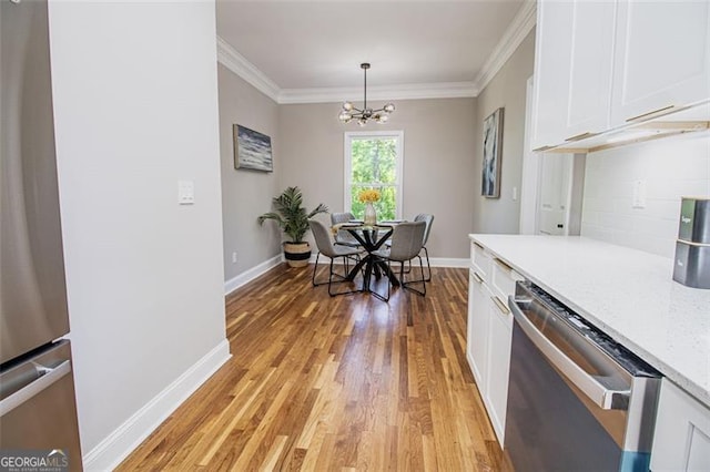 kitchen with ornamental molding, stainless steel appliances, pendant lighting, an inviting chandelier, and white cabinets