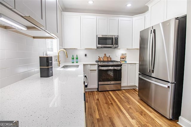 kitchen featuring sink, appliances with stainless steel finishes, tasteful backsplash, light hardwood / wood-style floors, and white cabinetry