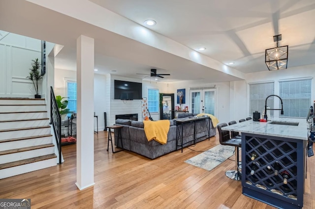 living room with french doors, a large fireplace, ceiling fan, sink, and light hardwood / wood-style flooring