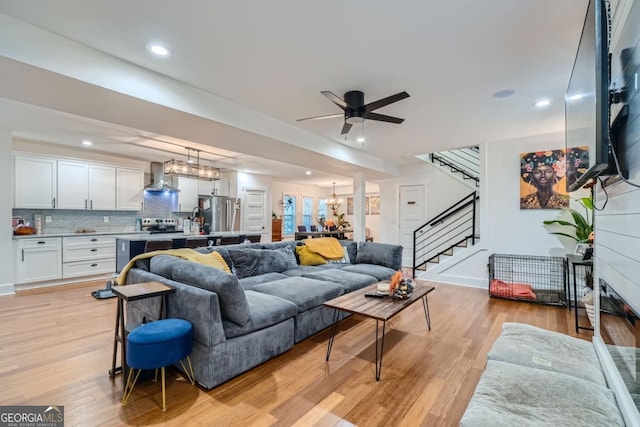 living room with ceiling fan with notable chandelier and light hardwood / wood-style flooring