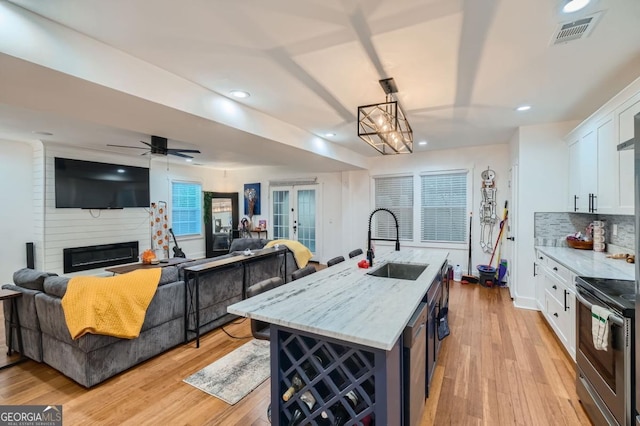 kitchen featuring sink, electric range, white cabinets, hanging light fixtures, and an island with sink