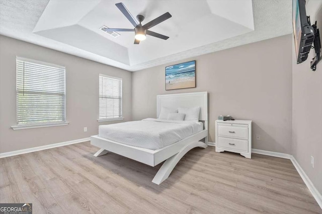 bedroom featuring a tray ceiling, ceiling fan, and light hardwood / wood-style floors