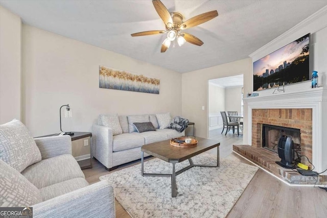 living room featuring ceiling fan, light hardwood / wood-style flooring, and a brick fireplace