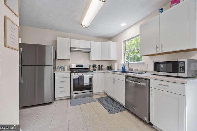 kitchen featuring appliances with stainless steel finishes, a textured ceiling, sink, light tile patterned floors, and white cabinetry