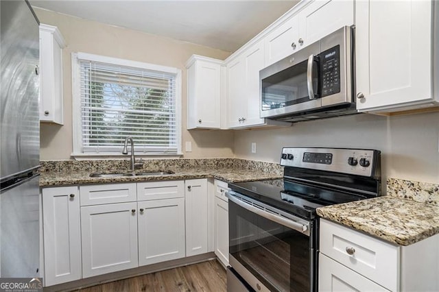 kitchen featuring appliances with stainless steel finishes, light stone counters, sink, wood-type flooring, and white cabinets