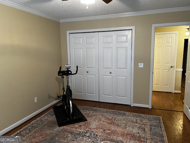 exercise room with a textured ceiling, dark wood-type flooring, ceiling fan, and crown molding