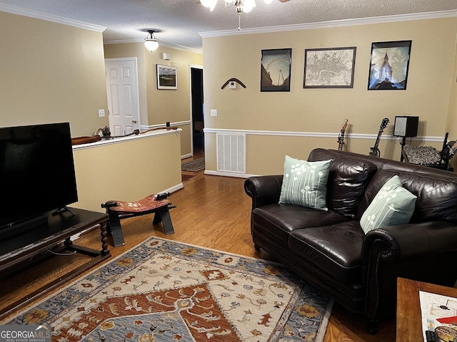 living room featuring ceiling fan, wood-type flooring, a textured ceiling, and ornamental molding