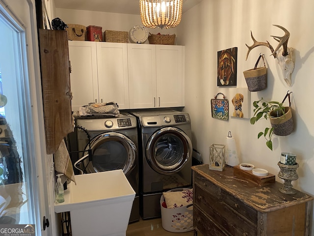 clothes washing area featuring washing machine and dryer, cabinets, and an inviting chandelier