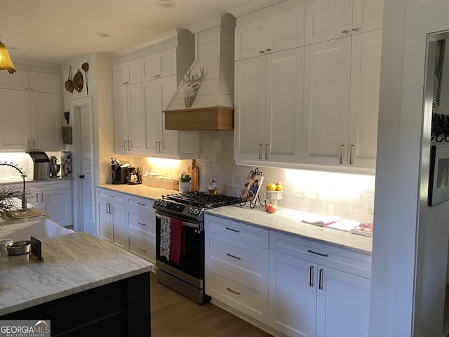 kitchen featuring light wood-type flooring, backsplash, stainless steel gas range, custom range hood, and white cabinetry