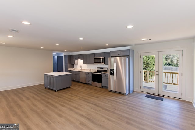 kitchen featuring appliances with stainless steel finishes, light wood-type flooring, french doors, gray cabinetry, and a kitchen island