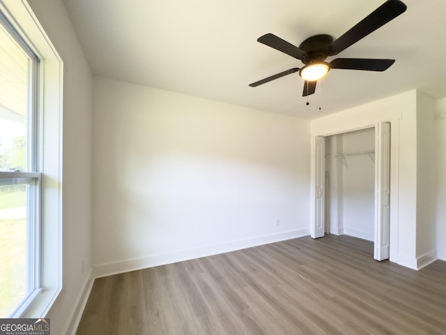 unfurnished bedroom featuring ceiling fan, a closet, wood-type flooring, and multiple windows