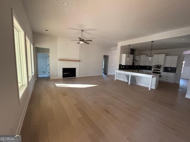 unfurnished living room with a large fireplace, baseboards, light wood-style flooring, and a ceiling fan