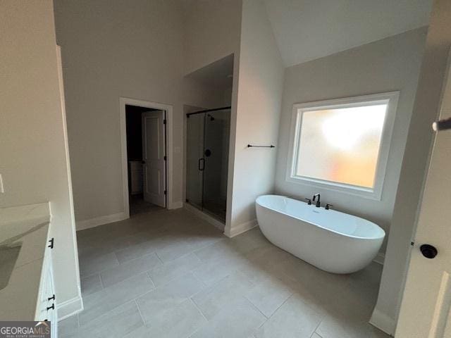 bathroom with a stall shower, tile patterned floors, vaulted ceiling, vanity, and a freestanding tub