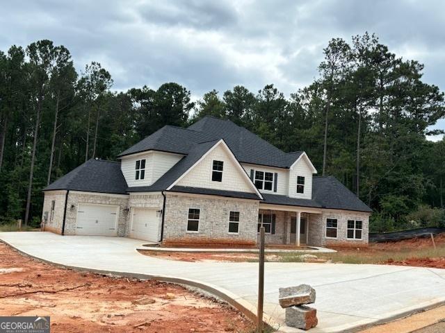 view of front of property featuring a garage, stone siding, a forest view, and concrete driveway