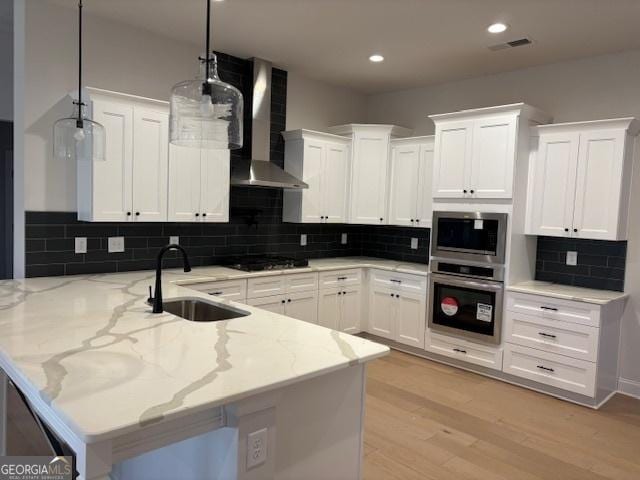 kitchen with visible vents, a peninsula, black stovetop, wall chimney range hood, and a sink