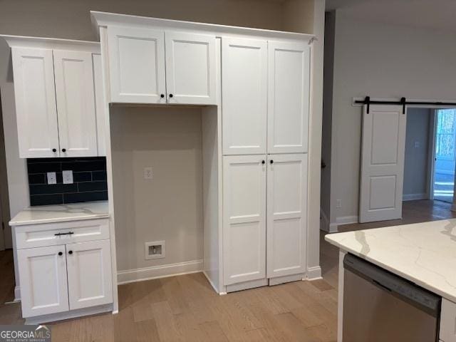 kitchen featuring light wood finished floors, a barn door, white cabinets, light stone counters, and stainless steel dishwasher