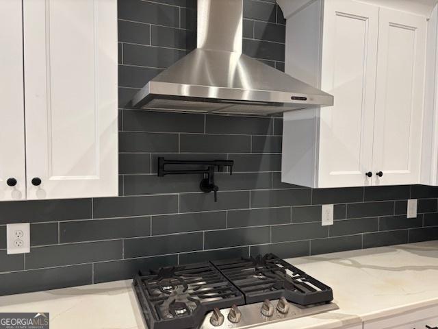 kitchen featuring white cabinetry, wall chimney range hood, range, light stone countertops, and tasteful backsplash