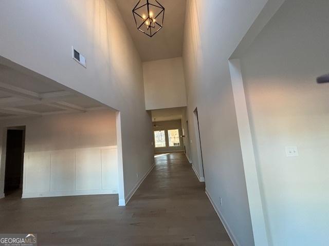 hall with a notable chandelier, visible vents, a towering ceiling, wood finished floors, and baseboards