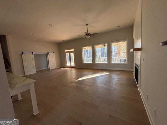 unfurnished living room with a barn door, baseboards, a ceiling fan, wood finished floors, and a fireplace