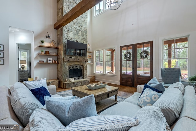 living room featuring french doors, a stone fireplace, plenty of natural light, and a high ceiling