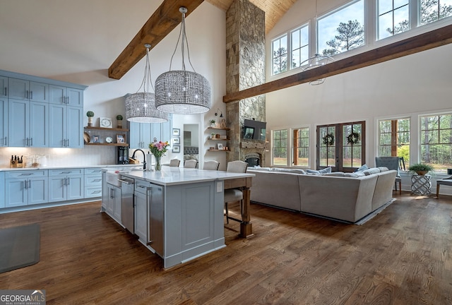 kitchen with a towering ceiling, backsplash, hanging light fixtures, a breakfast bar area, and an island with sink