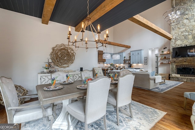 dining room featuring light wood-type flooring, beam ceiling, high vaulted ceiling, a fireplace, and a chandelier
