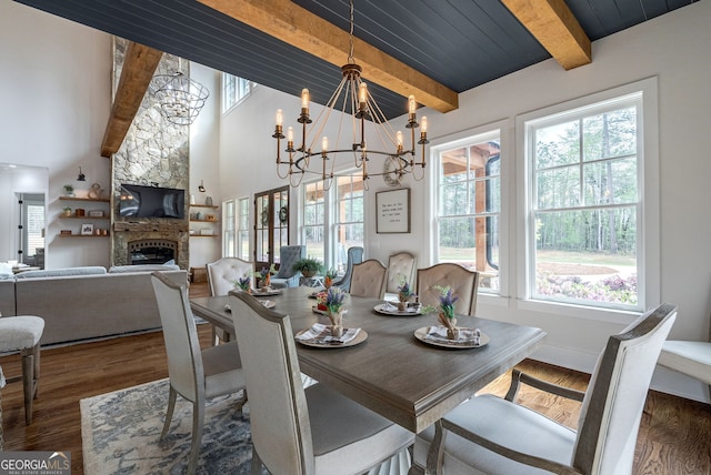 dining room with beam ceiling, a fireplace, a wealth of natural light, and an inviting chandelier
